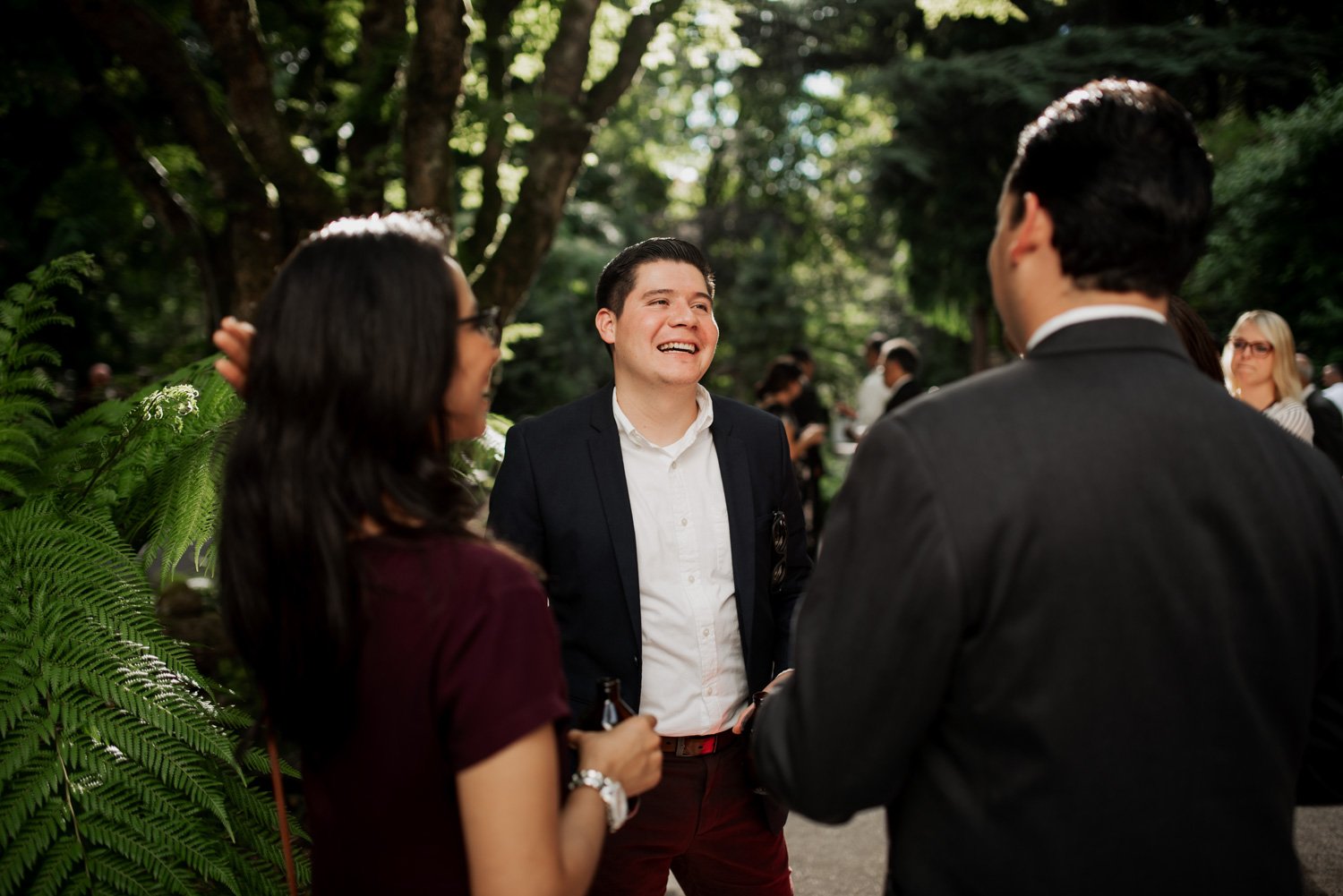 Three people engage in conversation outdoors at Leach Botanical Garden, surrounded by lush green foliage; one person is smiling broadly.
