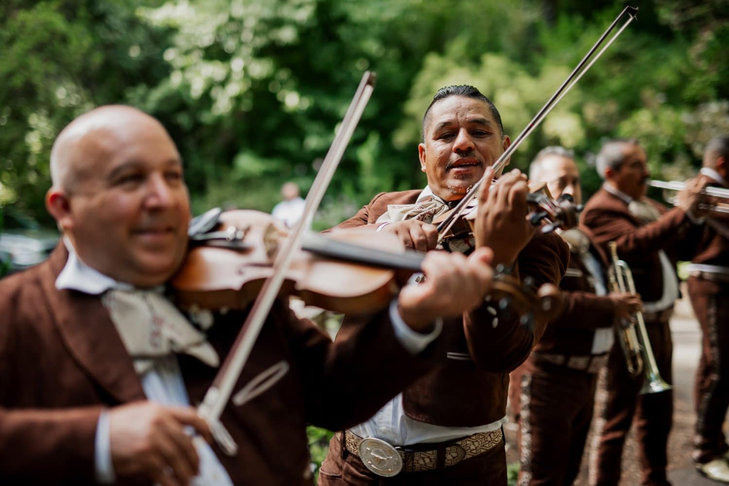 A mariachi band plays violins outdoors at a Leach Botanical Garden wedding, surrounded by lush greenery and enchanting guests.