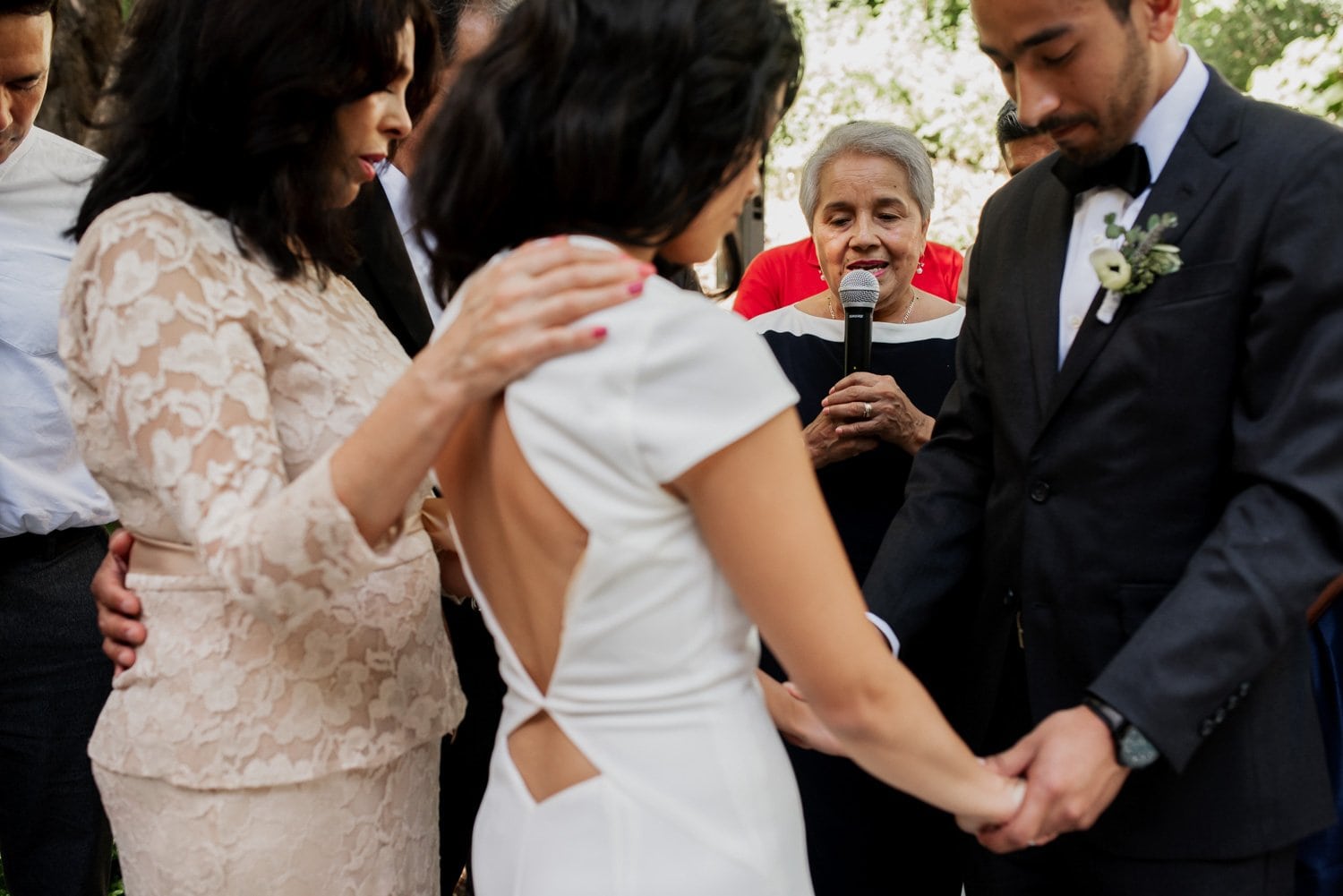 Guests gather in a circle, holding hands as vows are exchanged into a microphone at a Leach Botanical Garden wedding, amidst lush greenery and natural surroundings.