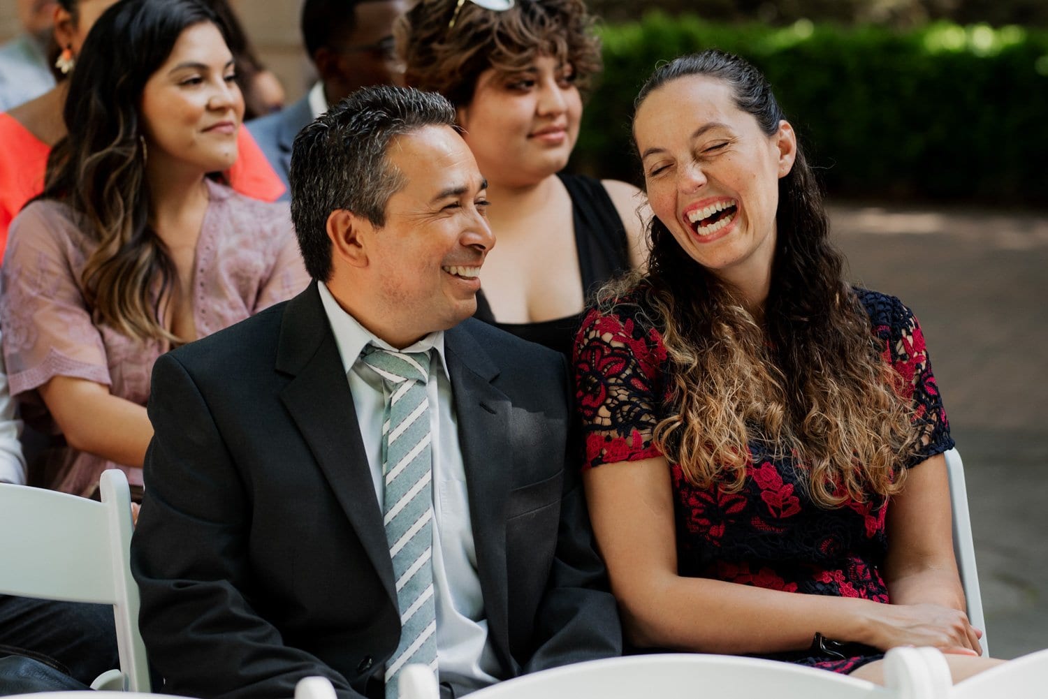 Guests at a Leach Botanical Garden wedding sitting outdoors, smiling and chatting among the lush green plants and trees.