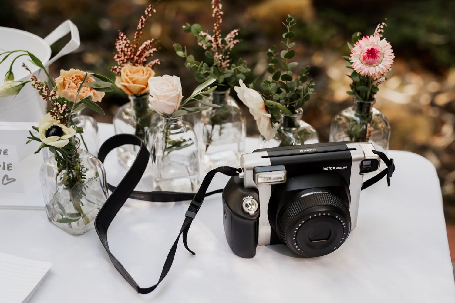 A Polaroid camera on a table surrounded by small vases with assorted flowers at a wedding in Leach Botanical Garden.