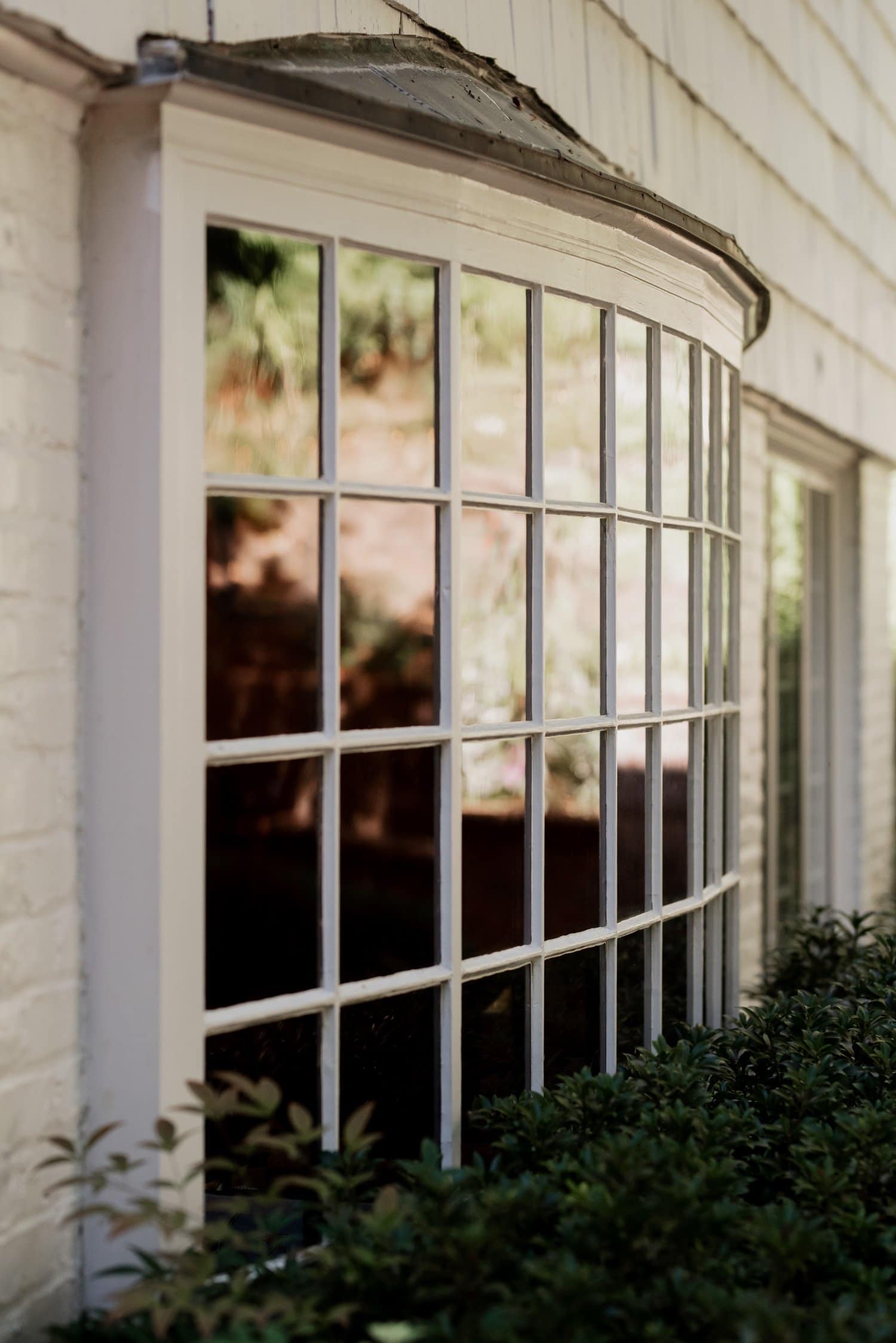 Close-up of a large curved window with grid panes on a white building at Leach Botanical Garden, surrounded by lush greenery.