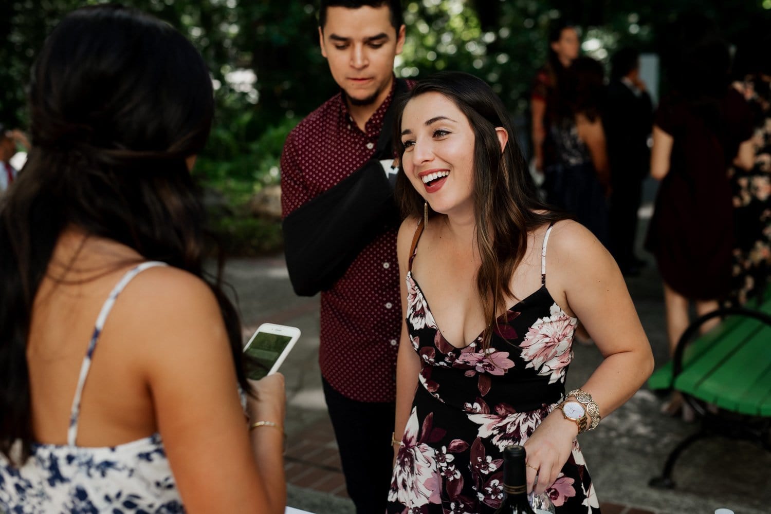 Woman in floral dress smiling and chatting with friends outdoors at Leach Botanical Garden during a wedding.