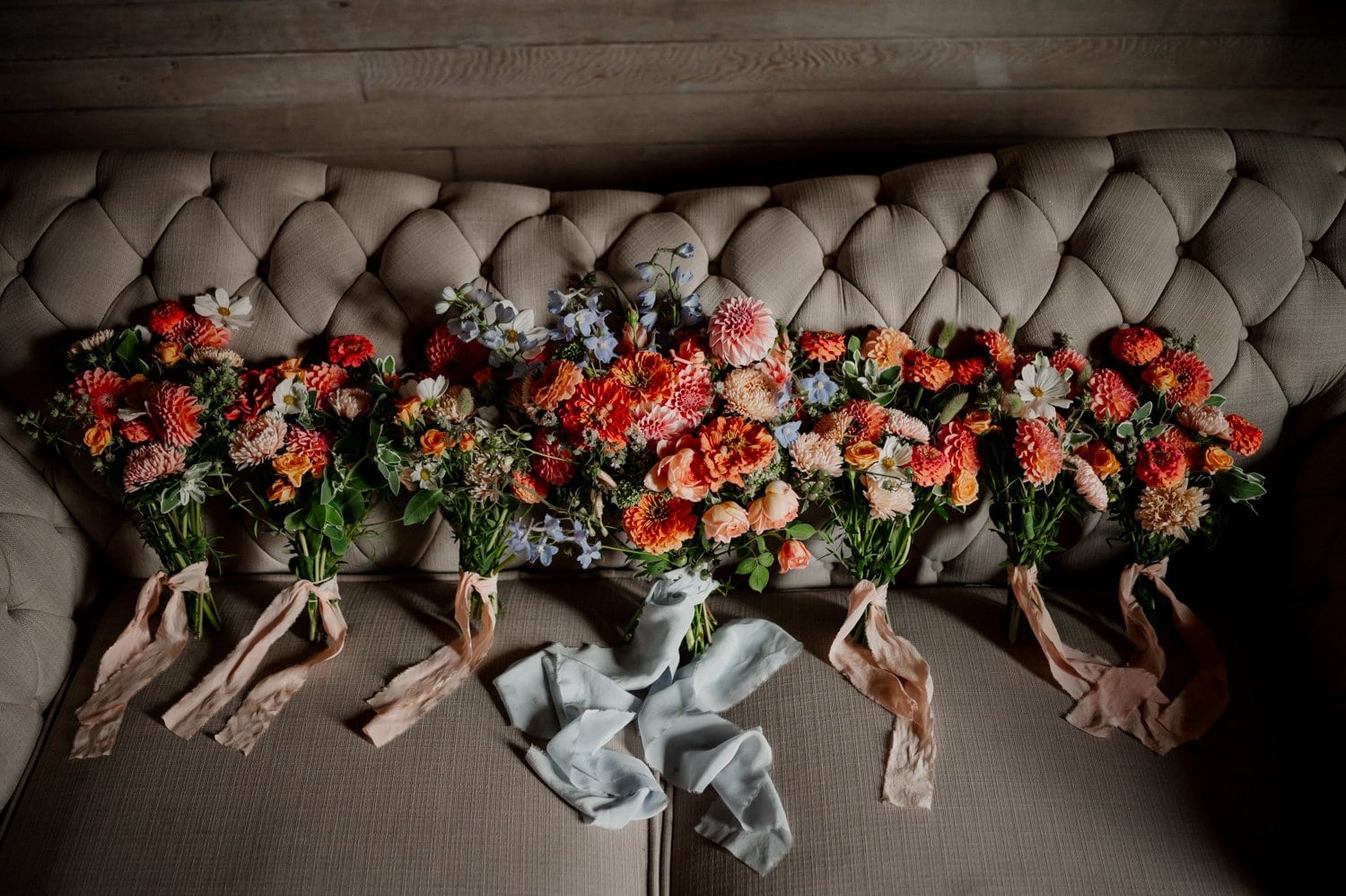 Bouquets of vibrant flowers with ribbons, perfect for a Cape Horn Estate wedding, are elegantly arranged on a tufted beige sofa.