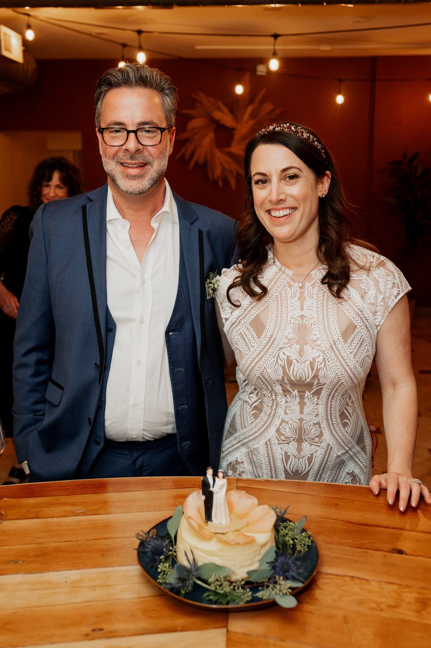A couple stands smiling behind a decorated cake at Opal 28s indoor venue.