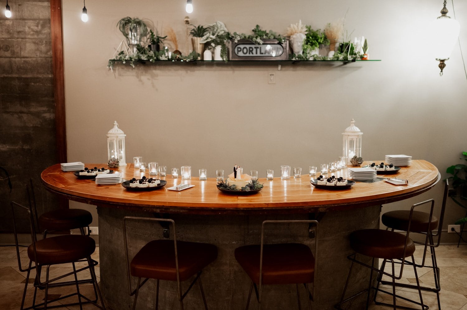 A cozy dining area featuring a semi-circular table surrounded by chairs, adorned with green plants, lit candles, and plates filled with pastries, creating an intimate setting suitable for a wedding at Opal 28.