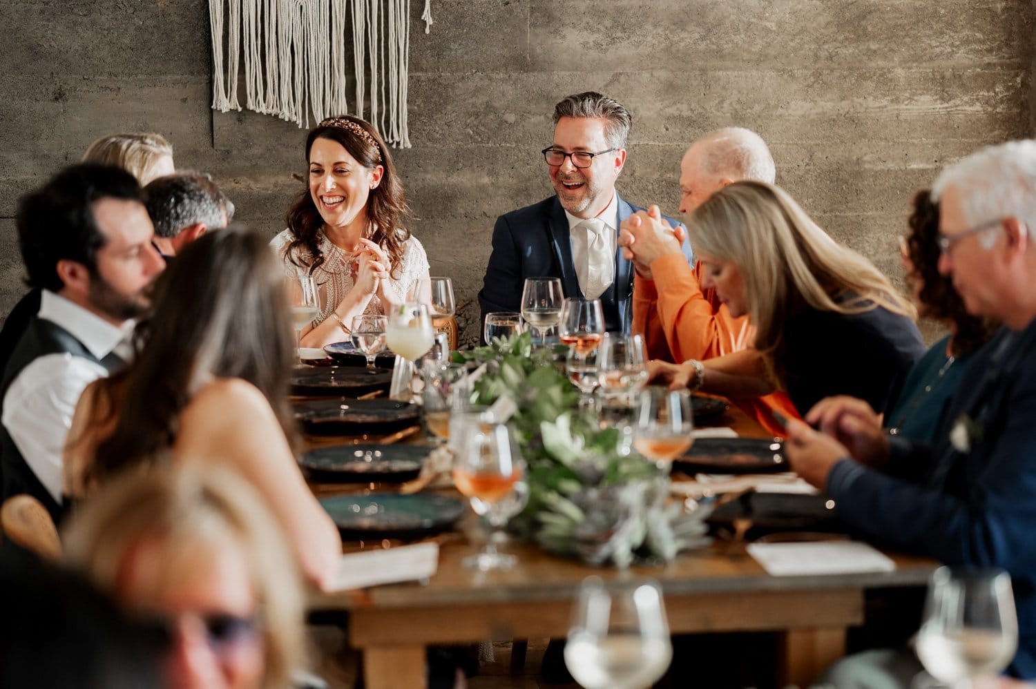 Guests gathered and conversed around a beautifully set banquet table, featuring wine glasses and a vibrant green centerpiece, at an unforgettable wedding held at Opal 28.
