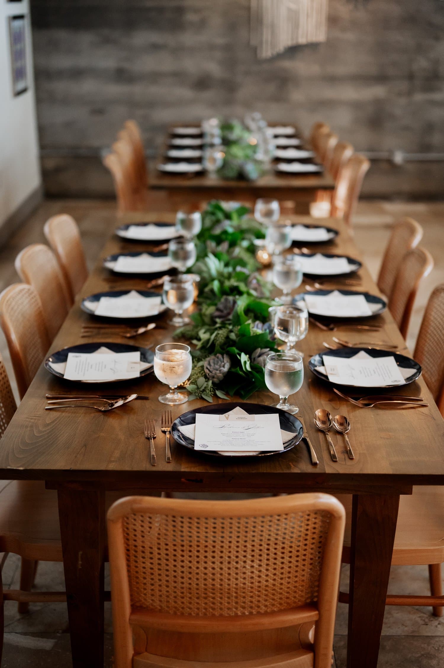 A long dining table at Opal 28 is set for a meal with neatly arranged plates, utensils, and a green leafy centerpiece, creating an intimate wedding celebration atmosphere.