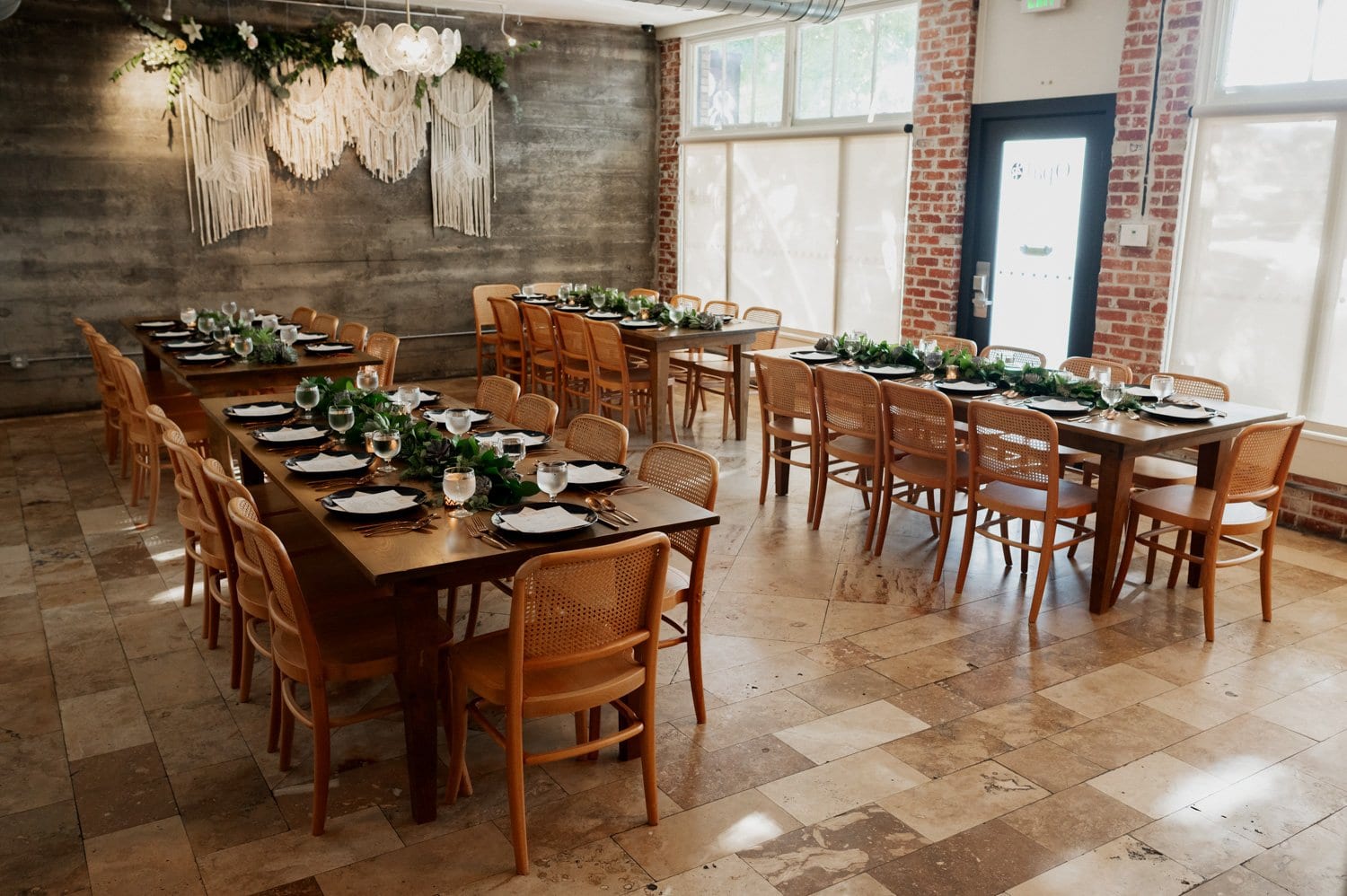 A rustic dining room features wooden tables and chairs, beautifully arranged for a gathering, with lush greenery and soft lighting creating an intimate ambiance suitable for a wedding at Opal 28.