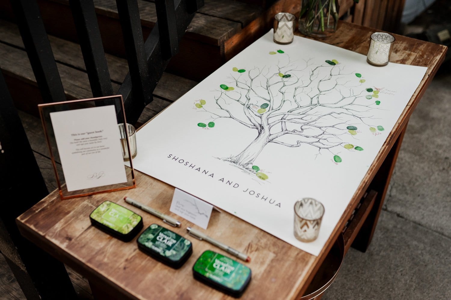 A wedding guestbook with a tree illustration is displayed on a table at Opal 28. Ink pads and flickering votive candles are arranged around it.