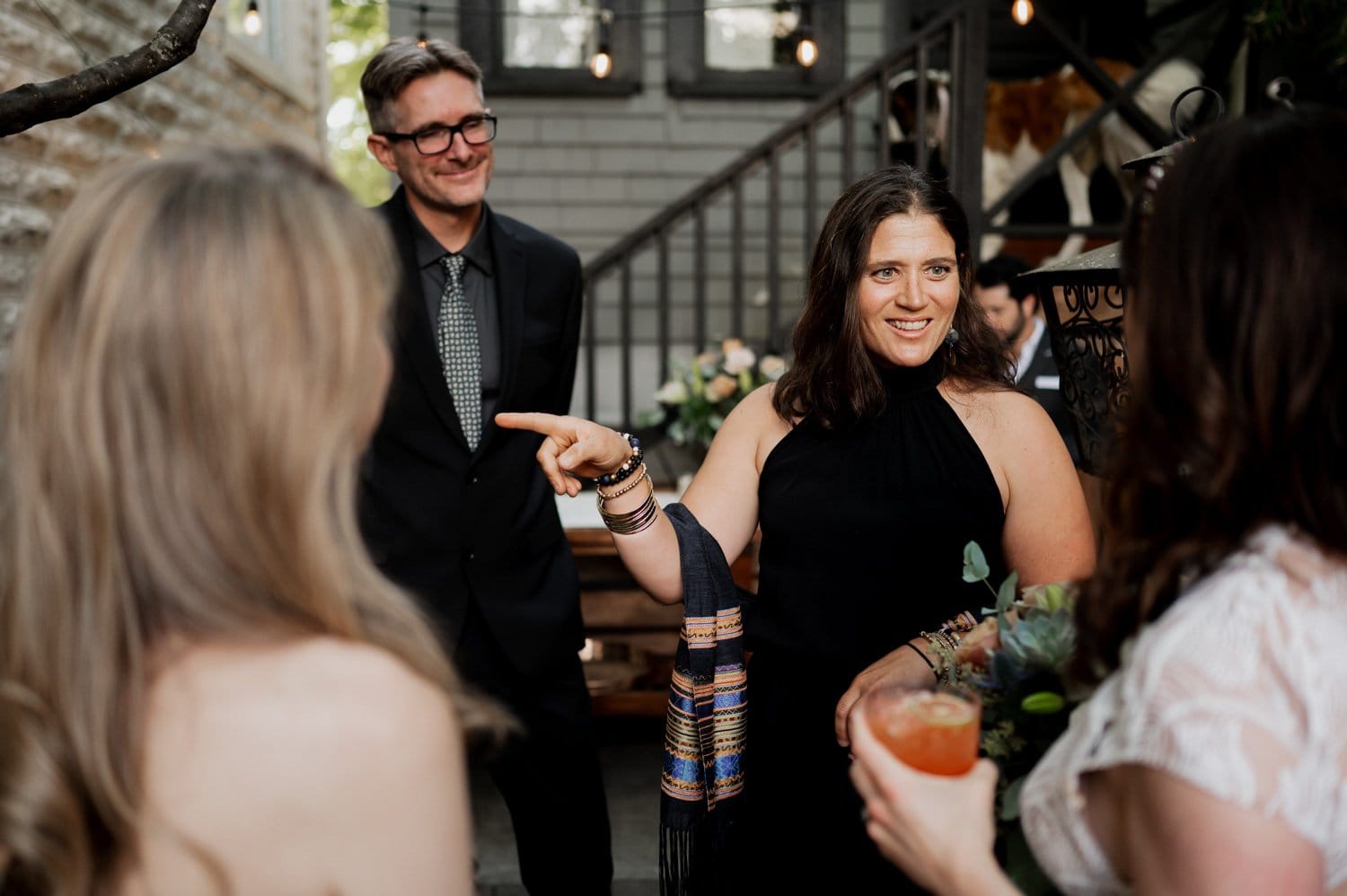 A group of people smiling and chatting at an outdoor gathering, with a woman joyfully holding a drink as they celebrate a vibrant wedding at Opal 28.
