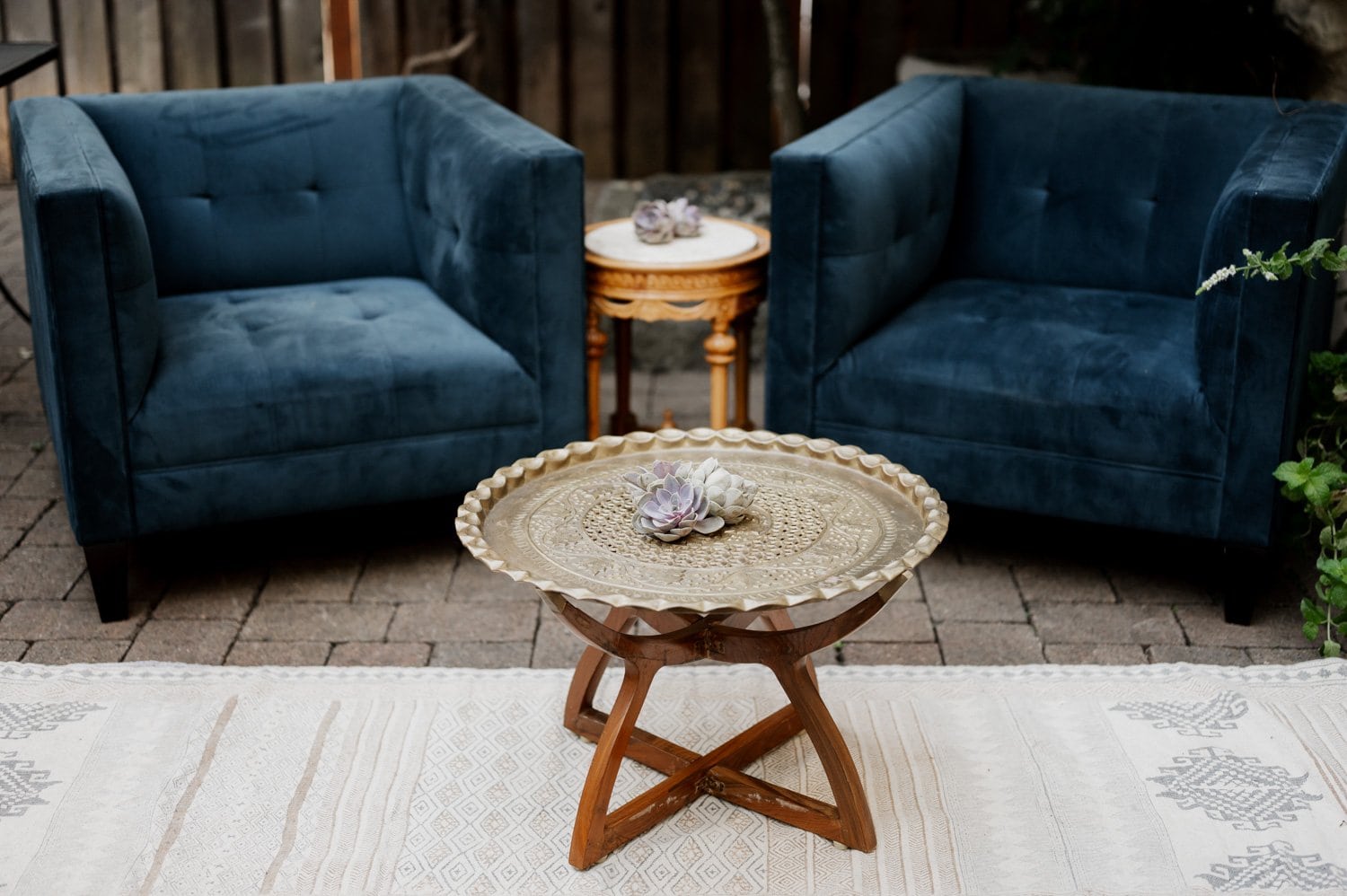 Two blue armchairs and a round wooden table with a decorative tray and succulent plant, set on a patterned rug, create an intimate setting at Opal 28.