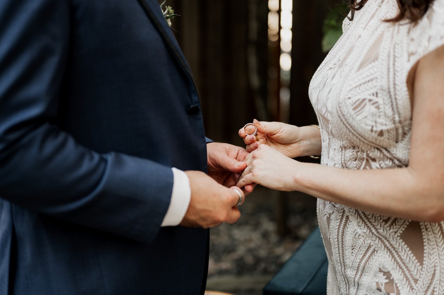 Close-up of a couple exchanging rings at their wedding at Opal 28, with the bride wearing a lace dress and the groom in a suit.