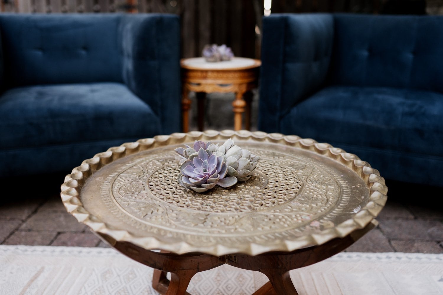 In a cozy setting, a round decorative table with a succulent centerpiece is placed between two blue sofas, suitable for an intimate gathering or wedding at Opal 28.