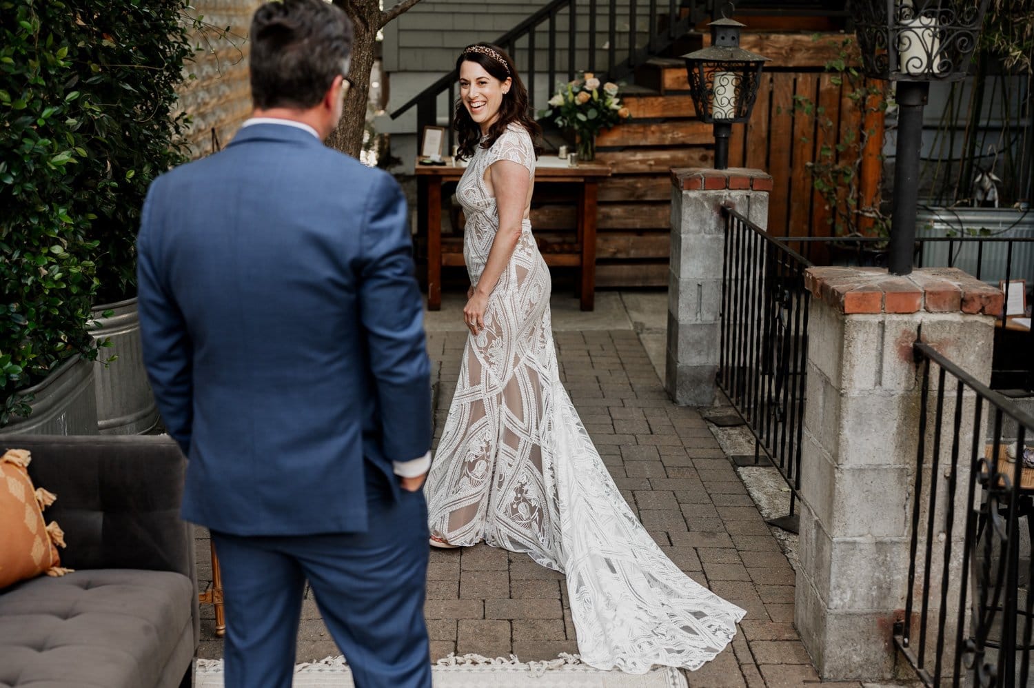 The bride in a lace gown smiles at the man in a blue suit as they stand on a patio with greenery and a staircase during their wedding at Opal 28.