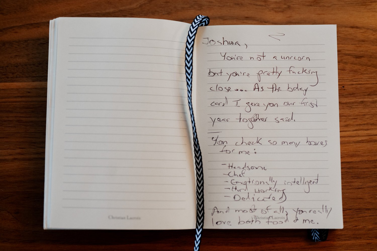 An open notebook sits on a wooden table in a cozy home in NE Portland, its pages filled with handwritten text. A black-and-white bookmark ribbon marks the thoughts of getting ready before the wedding at Opal 28.