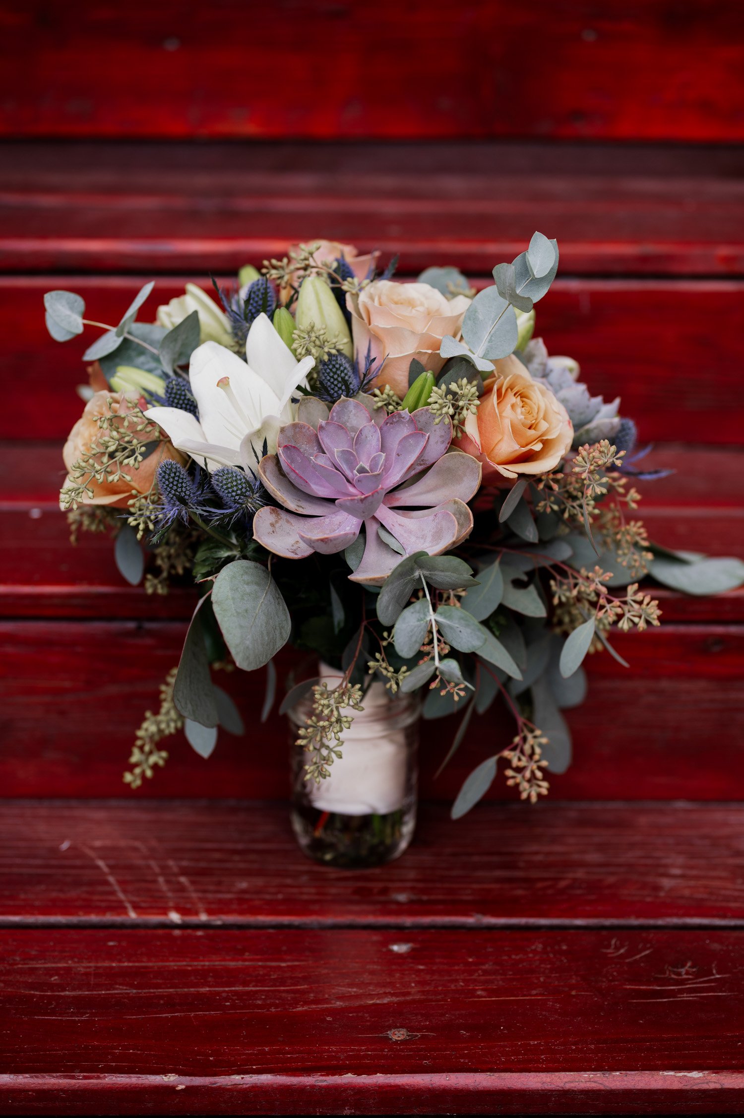 A bouquet with succulents, roses, and lilies sits elegantly in a glass vase on red wooden steps. Its a charming scene as a couple gets ready at home in NE Portland before their wedding at Opal 28.