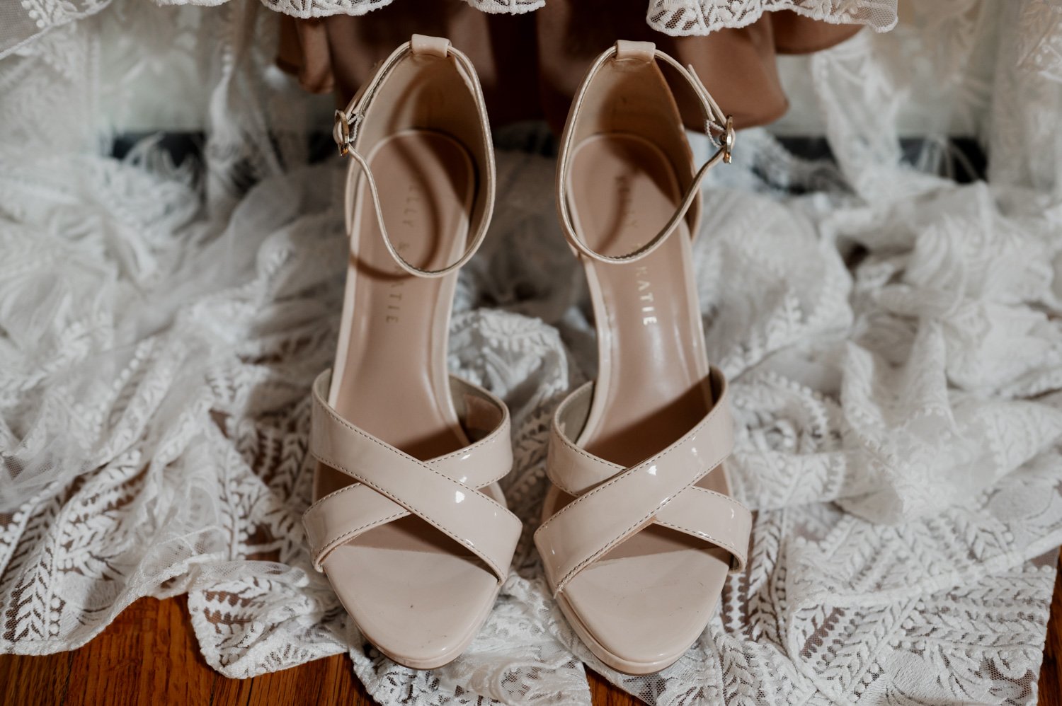 Beige strappy high-heeled shoes rest elegantly on a delicate white lace fabric background, capturing the essence of getting ready at a home in NE Portland before a wedding at Opal 28.