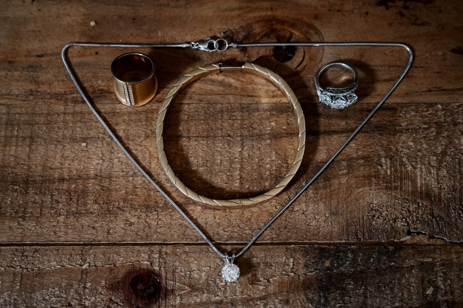 Jewelry set on wood: gold ring, silver ring, bracelet, and necklace with a pendant. Perfect for getting ready at a home in NE Portland before your wedding at Opal 28.