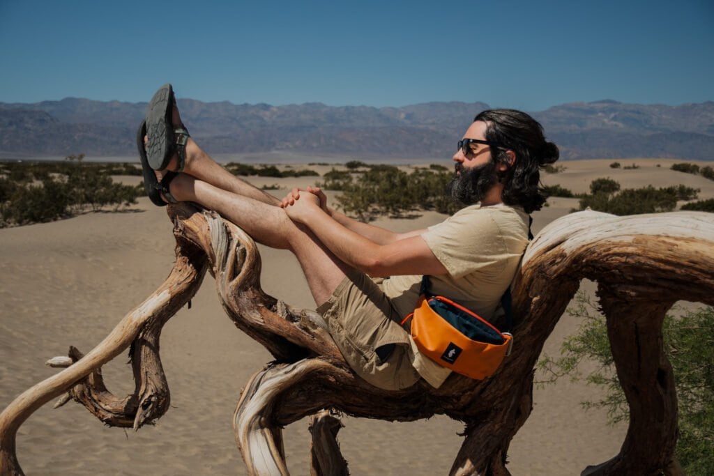 A portrait of Kyle Carnes, a Portland, Oregon, wedding and elopement photographer, lounging on a large weather tree root in Death Valley.