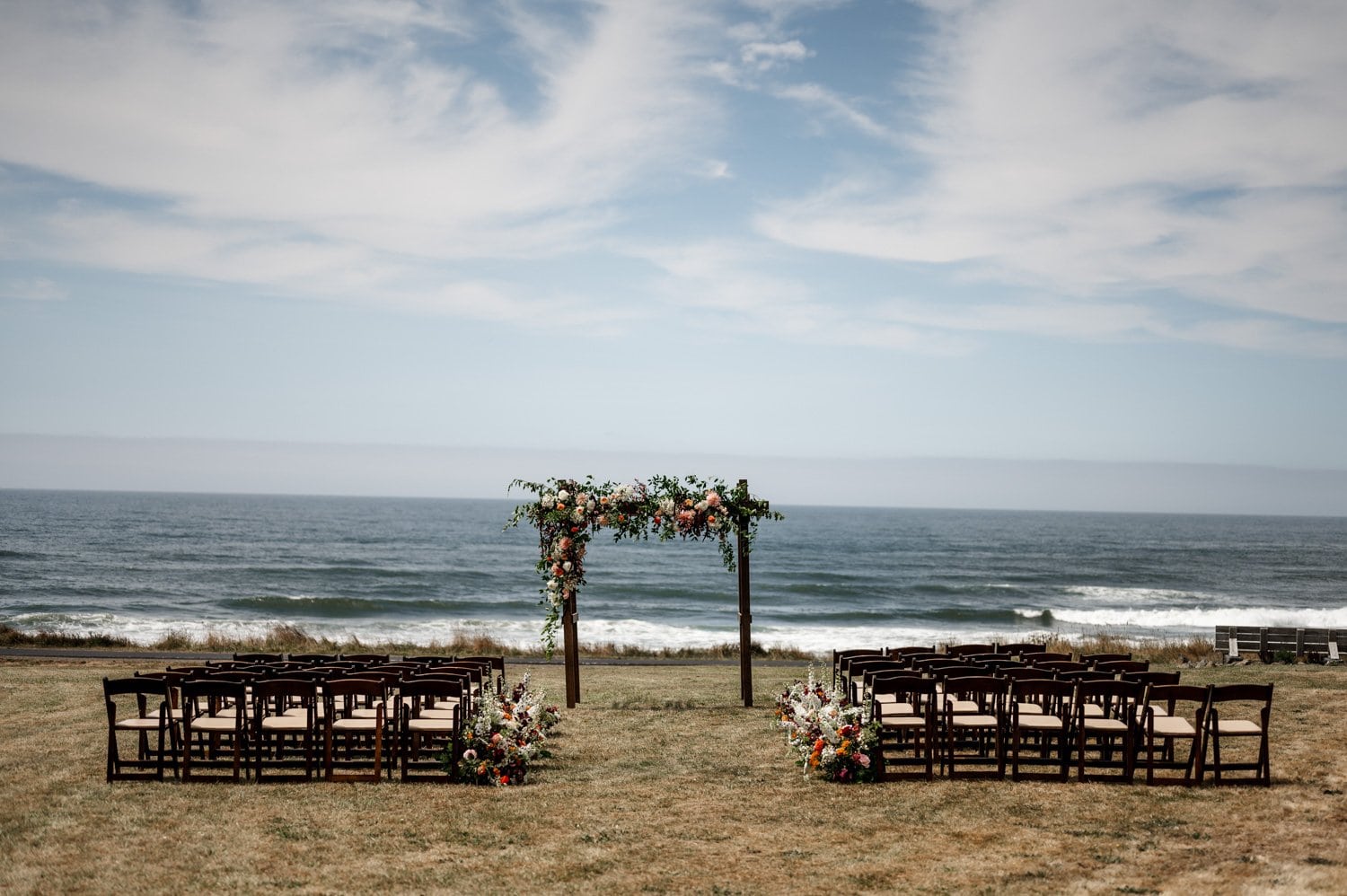 Outdoor wedding setup by the ocean, featuring rows of chairs and a floral arch on a grassy area at the Yachats Inn.