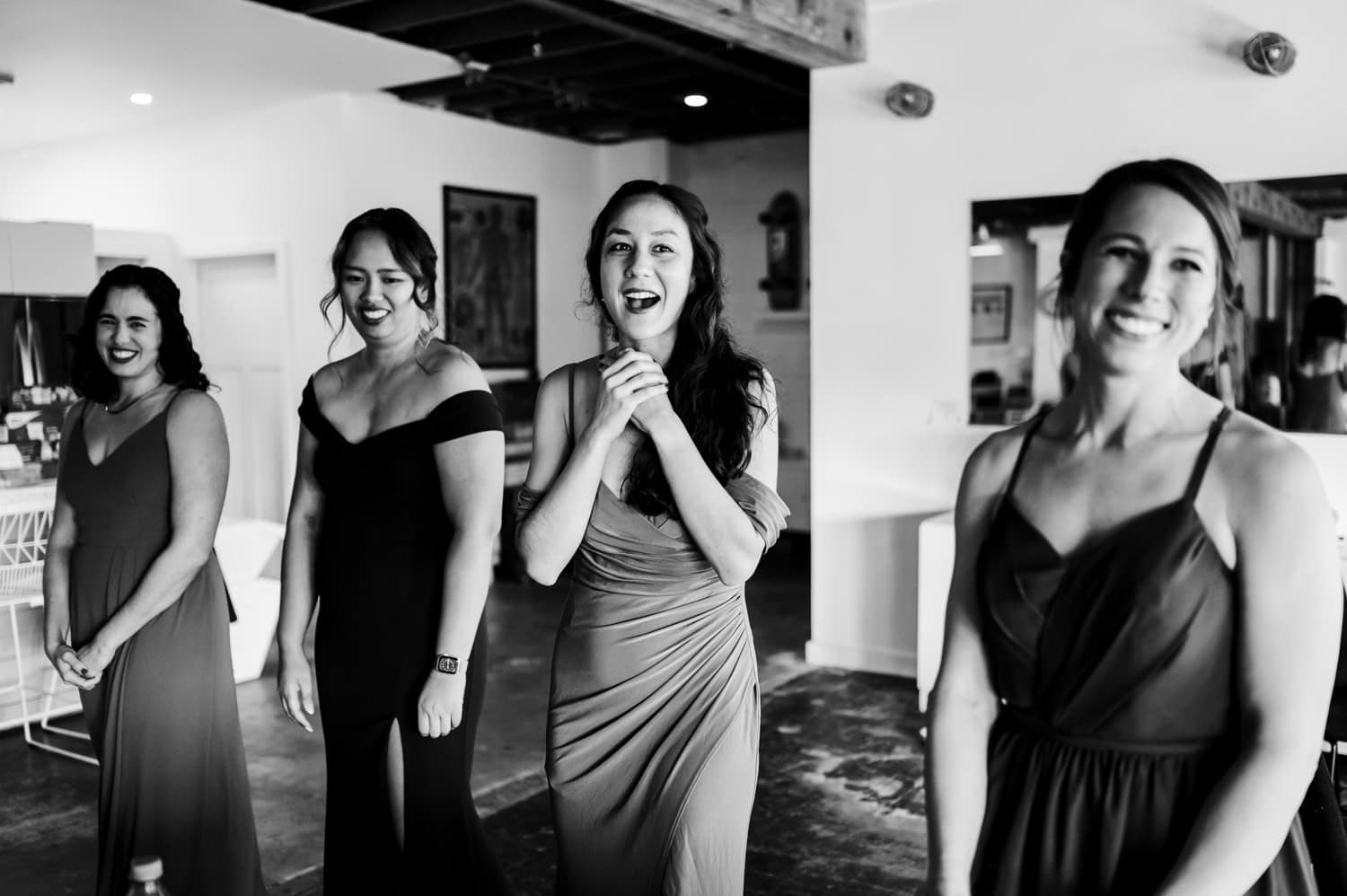 Four women in formal dresses smiling and laughing in a brightly lit room at Union/Pine during a wedding celebration.