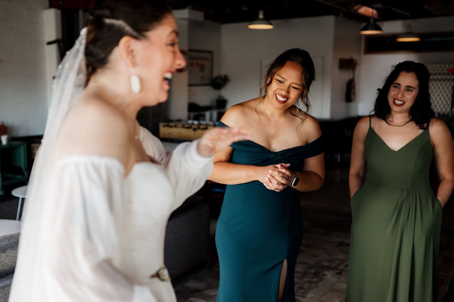 A bride laughing with two bridesmaids in green dresses inside the chic indoor setting of Union/Pine.