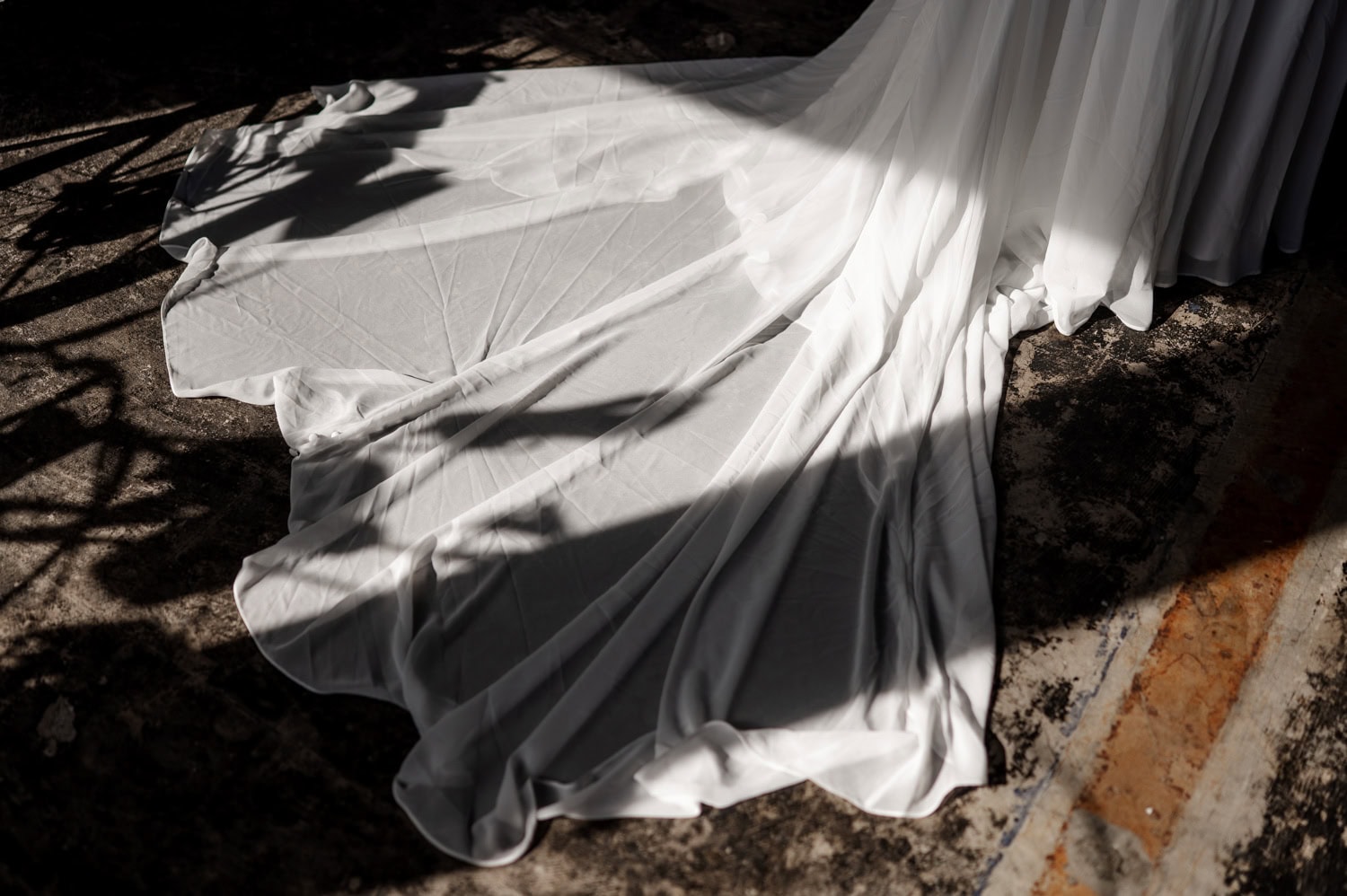 A white flowing dress with soft shadows gracefully drapes on a textured floor, highlighting the timeless beauty of a wedding at Union/Pine.