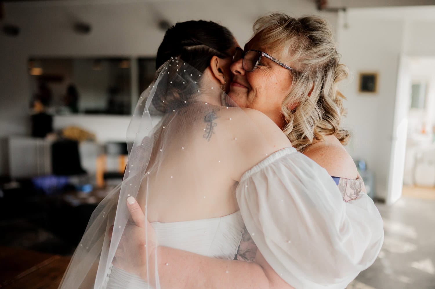 In a sunlit room at Union/Pine, the bride and an older woman hug warmly during the wedding.