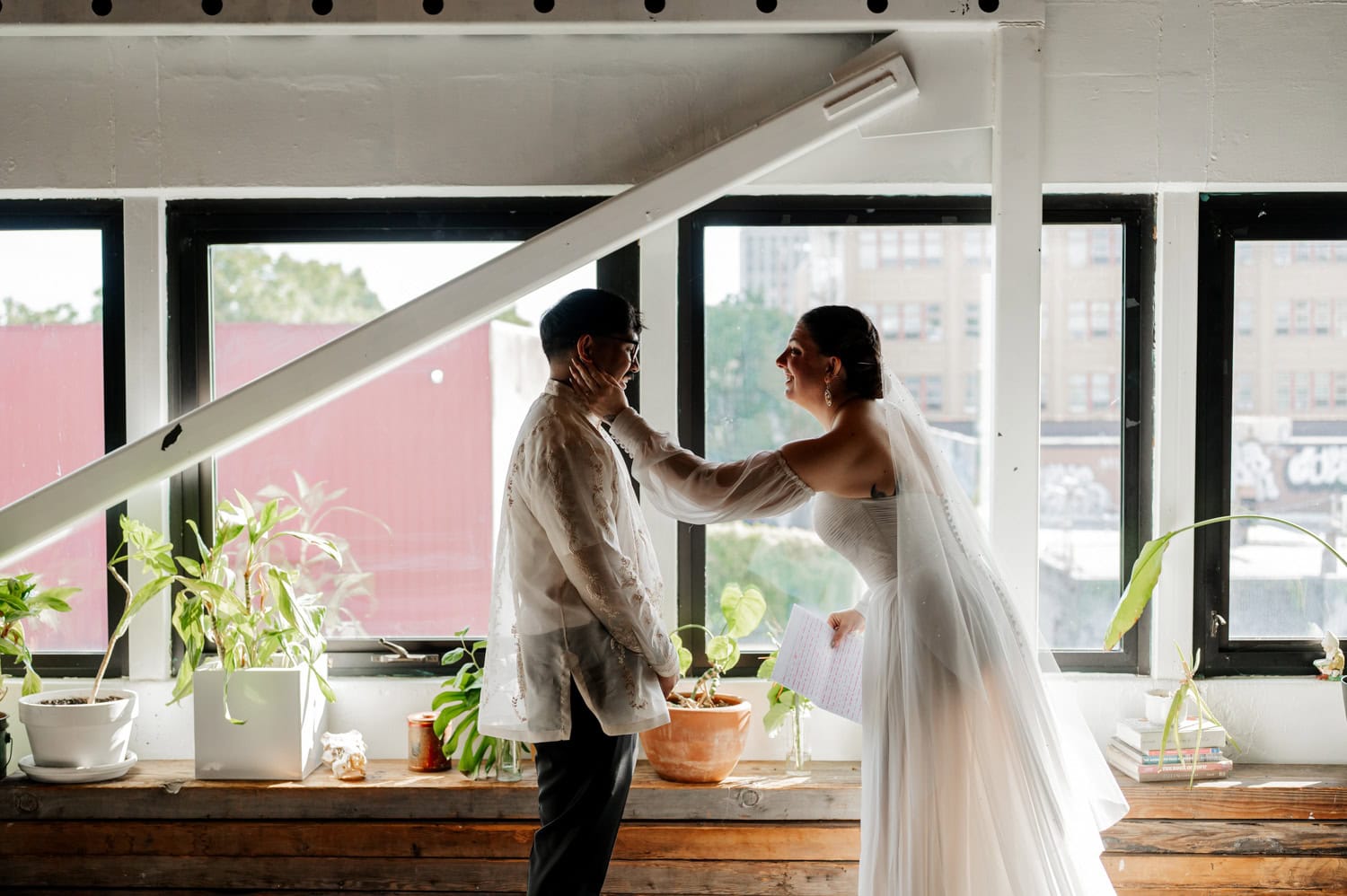 The bride and groom share a joyful smile, illuminated by sunlight, amidst vibrant greenery at their wedding at Union/Pine.