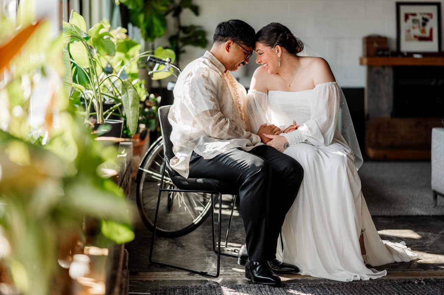 A couple in formal attire shares a tender moment, smiling and holding hands beside a wheelchair in a well-lit room. Both individuals exude happiness and connection.