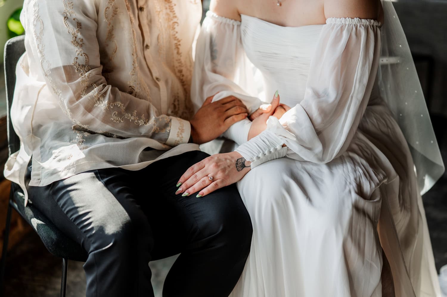 A couple in formal attire holds hands at Union/Pine; she wears a stunning white dress, and he wears an intricately embroidered shirt.