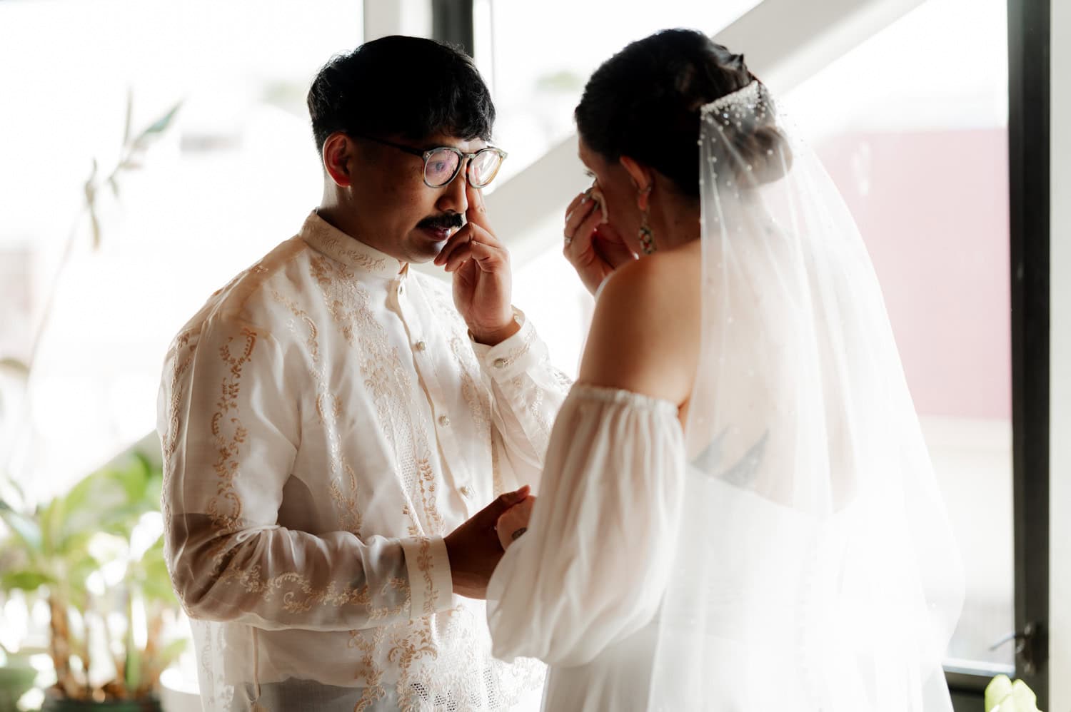 A bride and groom stand facing each other, holding hands in a well-lit room during their wedding at Union/Pine.