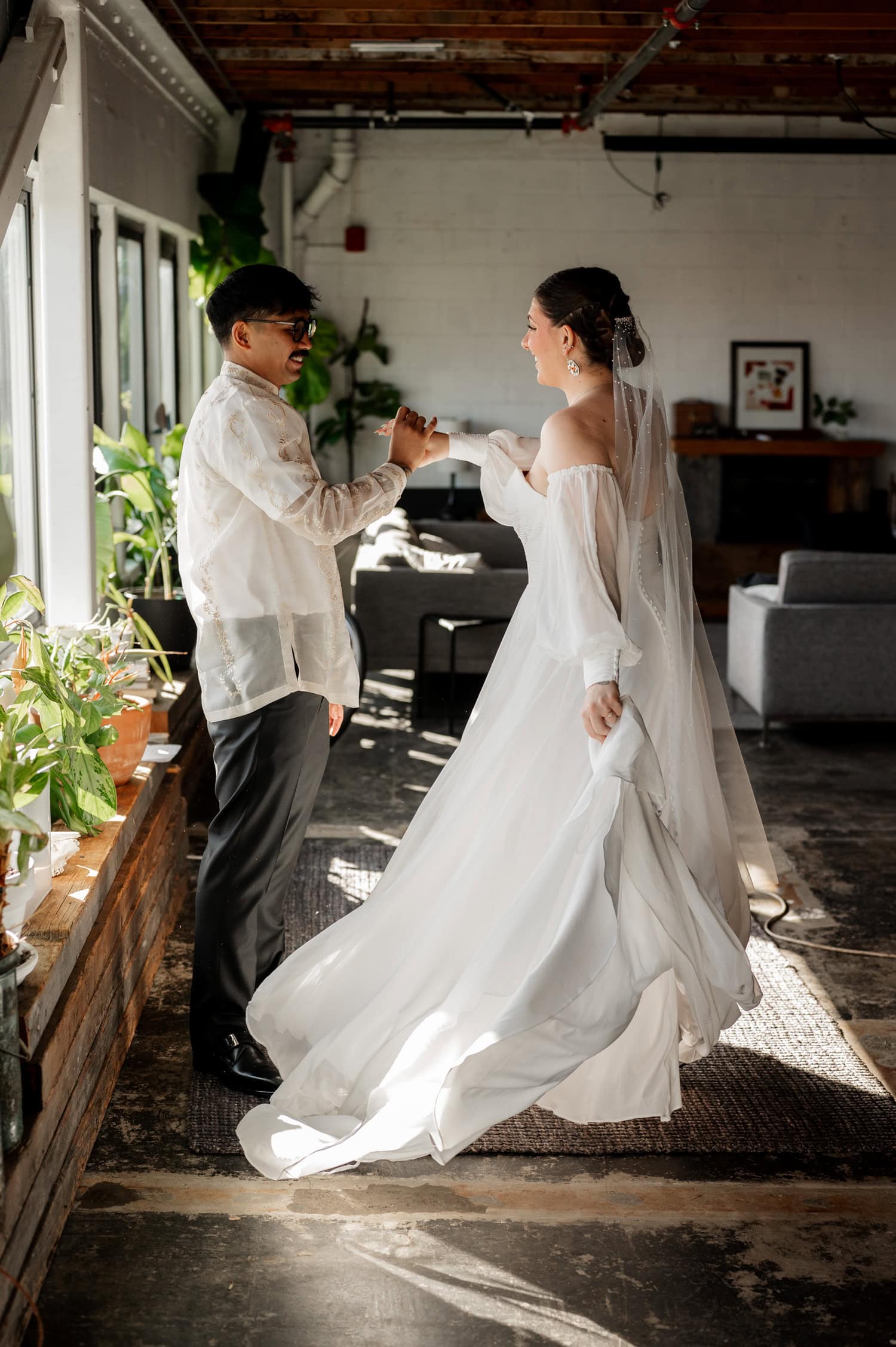 The bride and groom joyfully share a fist-bump in a sunlit room filled with plants and modern decor at Union/Pine.