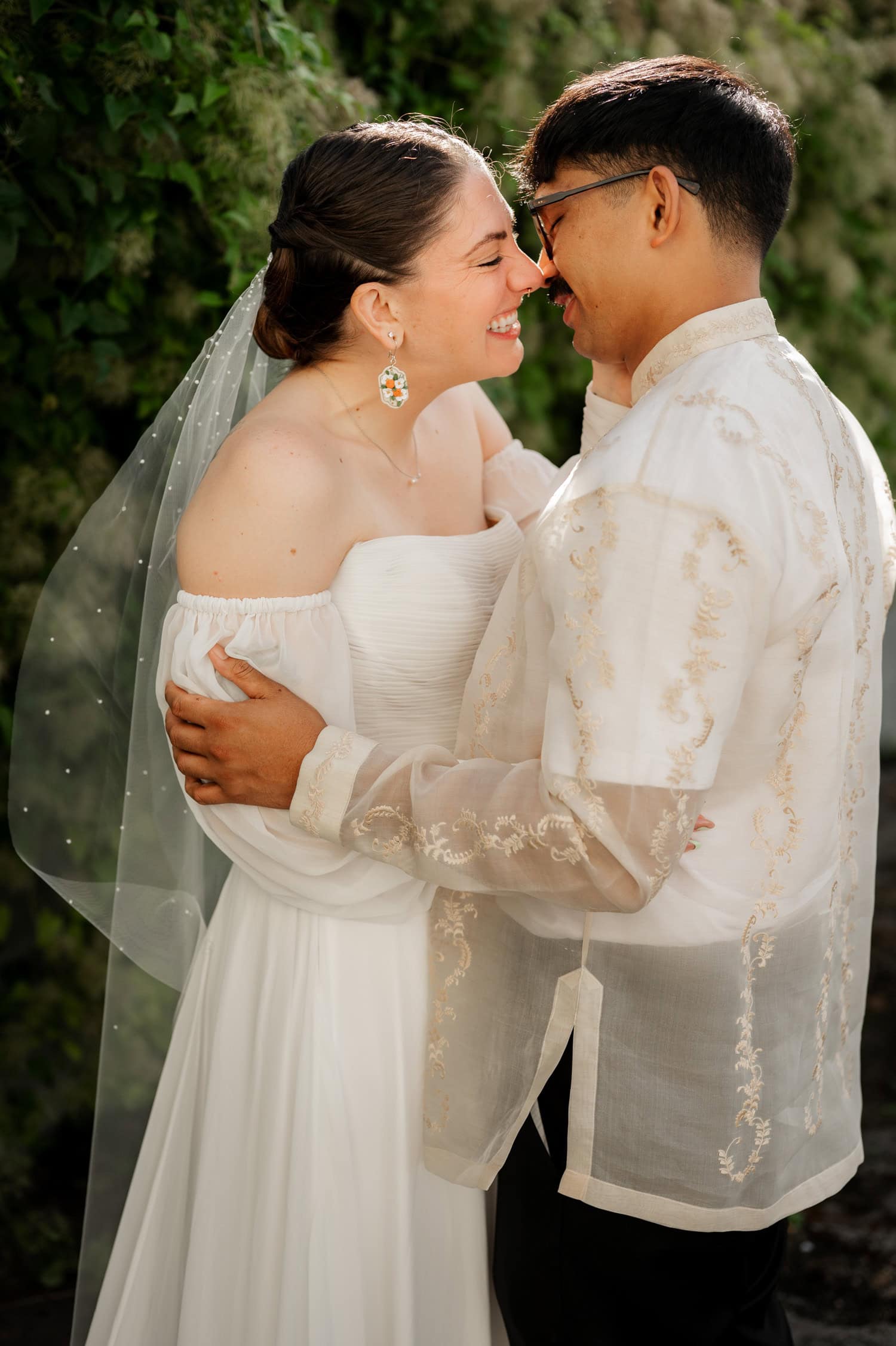 A couple in wedding attire embraces and smiles at each other against a lush, green backdrop during their wedding at Union/Pine.