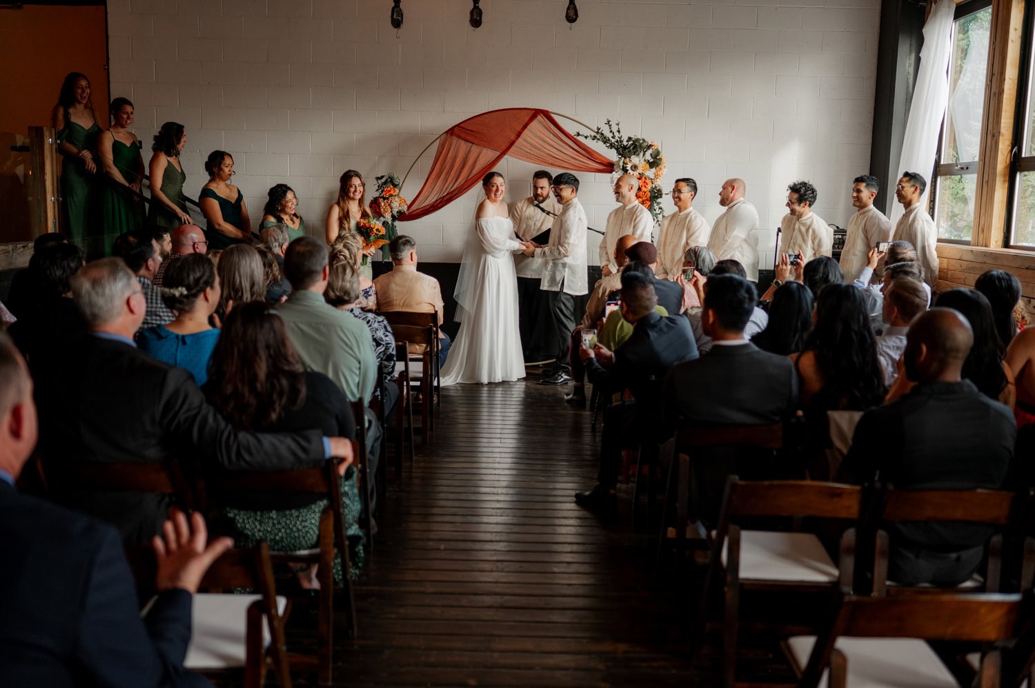 A wedding ceremony at Union/Pine with a couple standing at the altar, surrounded by their wedding party and guests seated in rows.