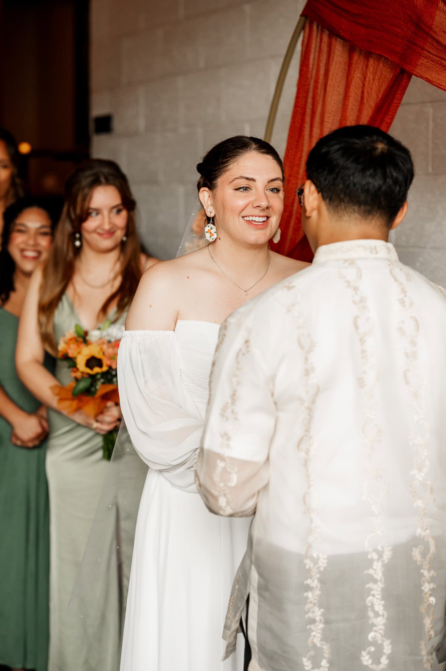 The bride and groom smile warmly at each other during their wedding at Union/Pine, with bridesmaids standing supportively around them.
