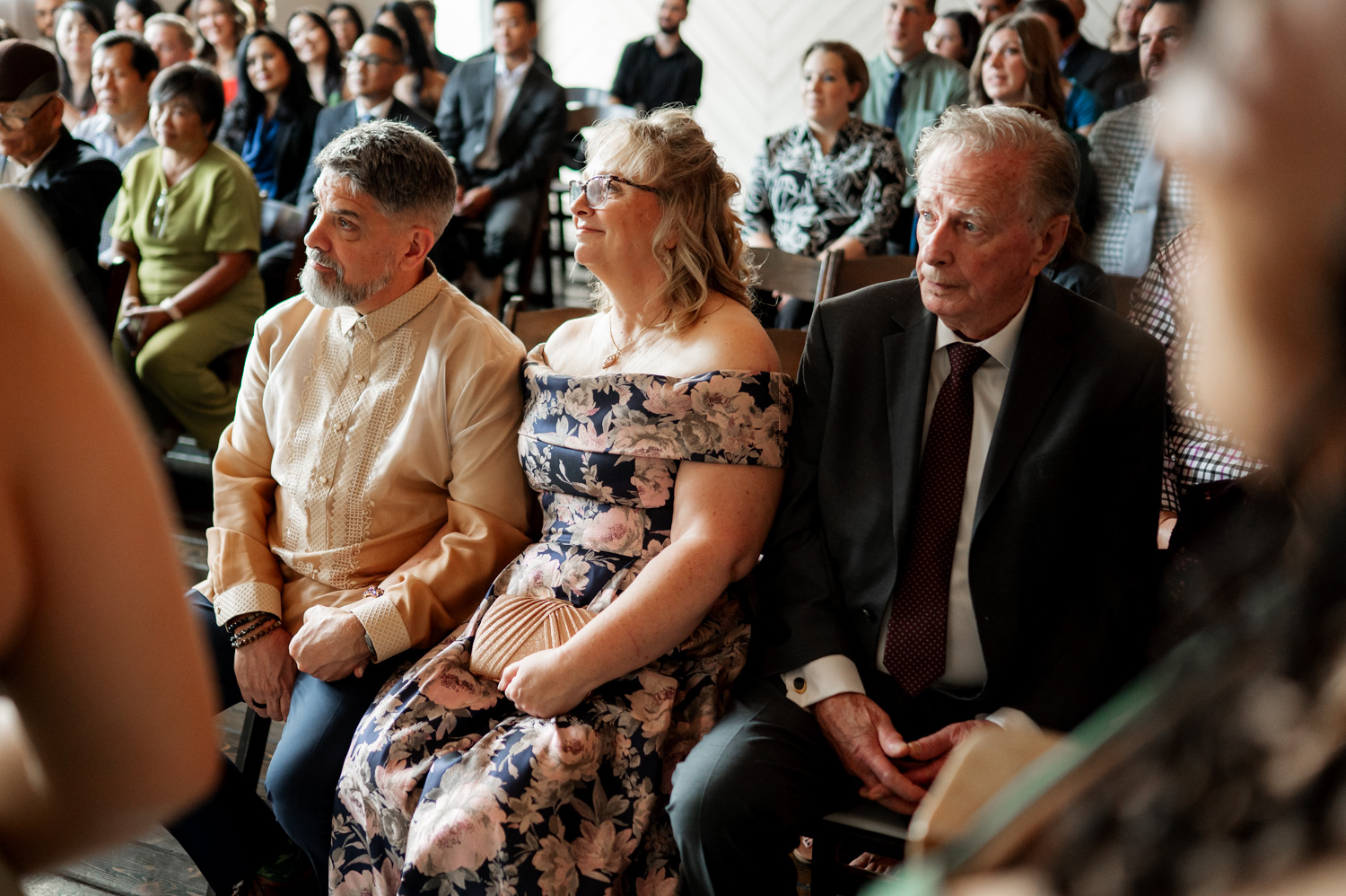 Guests at Union/Pine dressed in formal wedding attire, focus their attention on something off to the side.