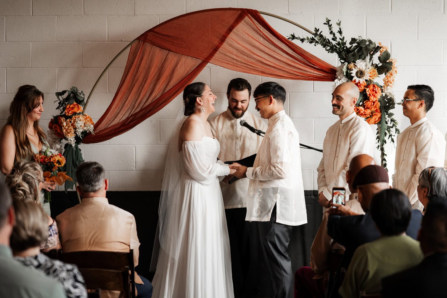 The bride and groom smile at each other during a wedding ceremony at Union/Pine, with their wedding party and guests gathered around.
