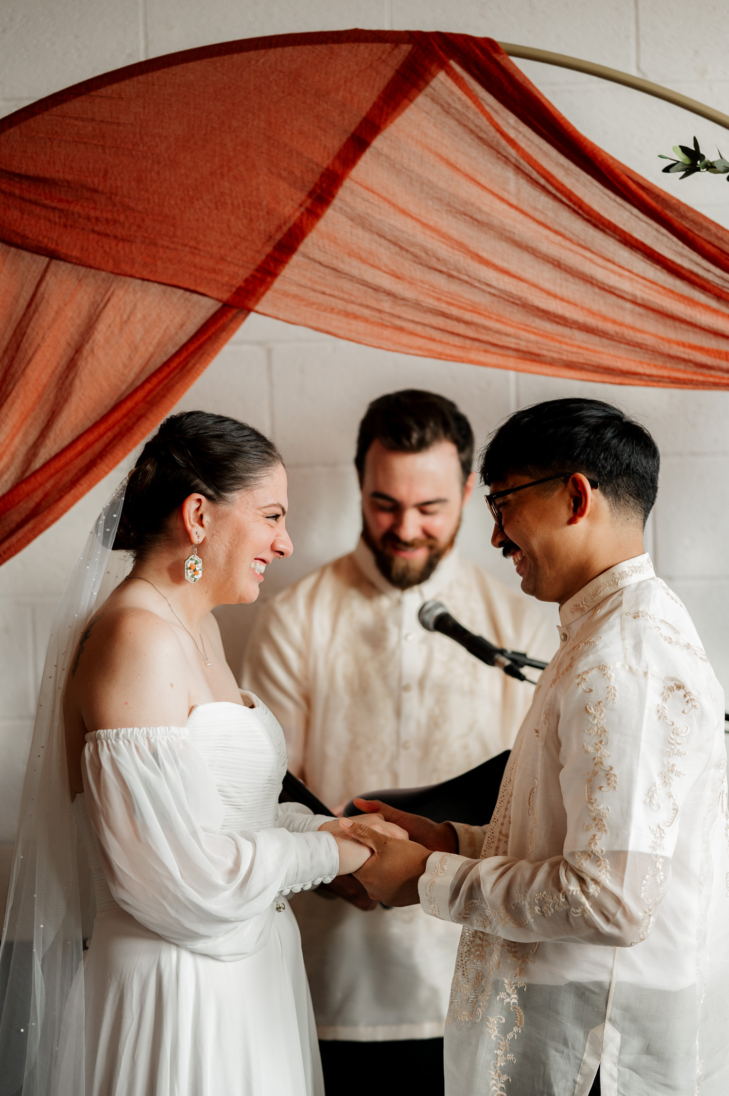 The bride and groom exchange joyful smiles during their wedding ceremony at Union/Pine, with the officiant standing behind them.