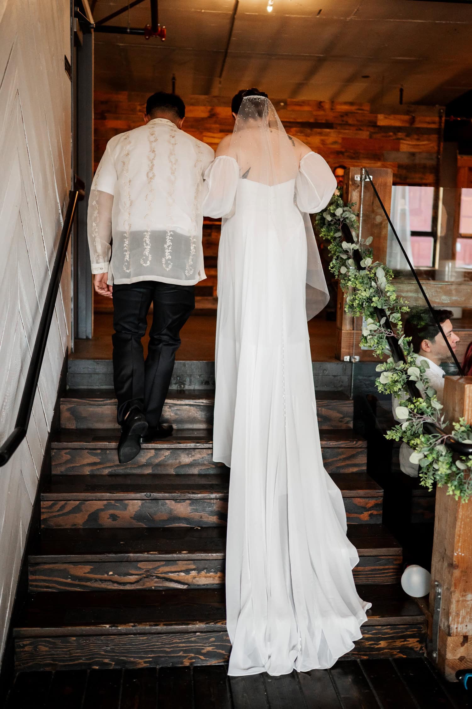 The bride and groom ascend wooden stairs decorated with flowers, creating an enchanting scene at their wedding venue Union/Pine.