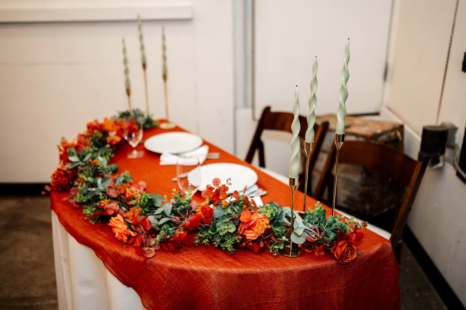 A table with an orange cloth, floral decor, two plates, and twisted candles set up for an intimate wedding at Union/Pine.