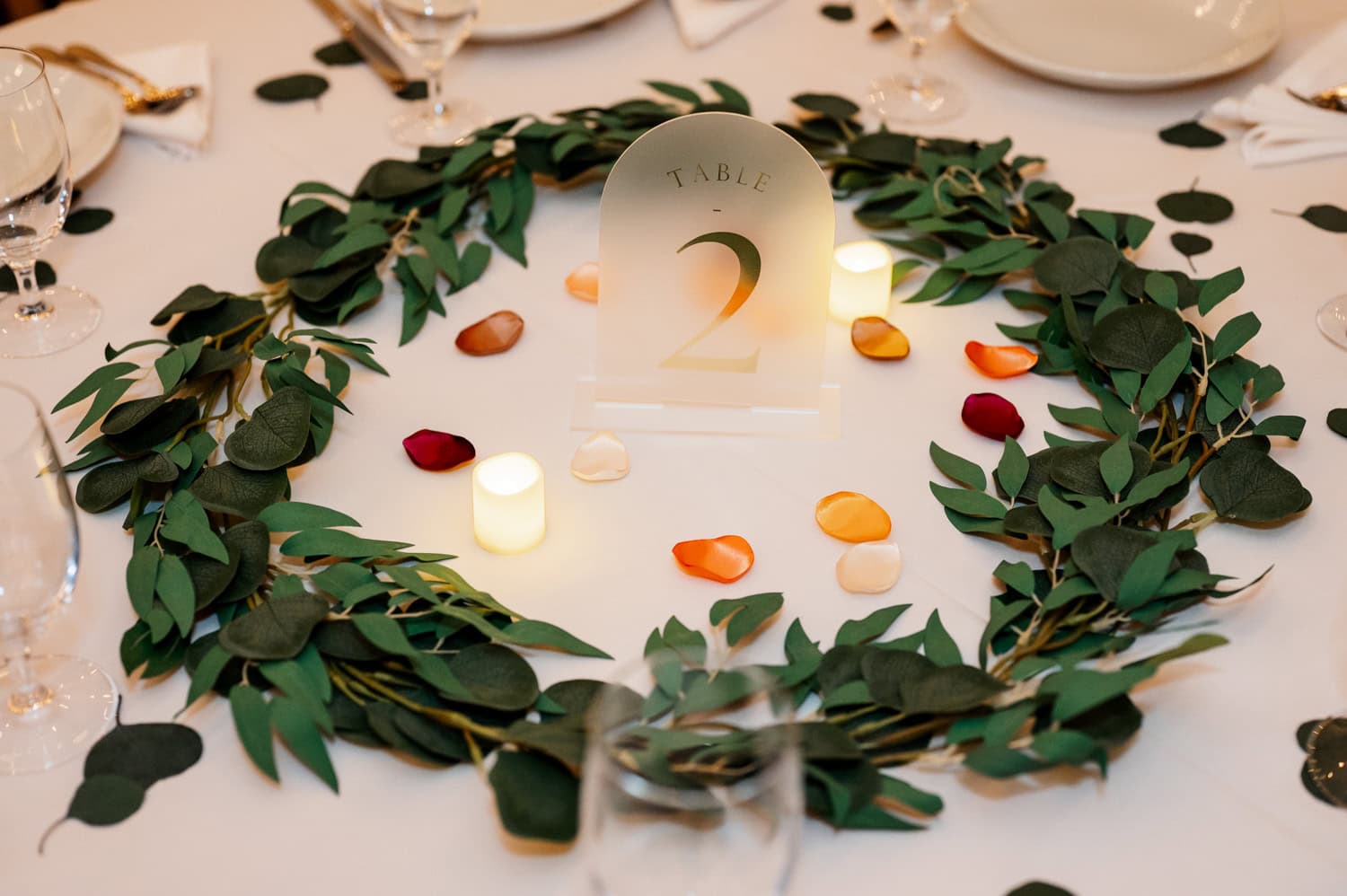 A table decorated with greenery, scattered rose petals, lit candles, and a Table 2 sign on a white tablecloth at Union/Pine.