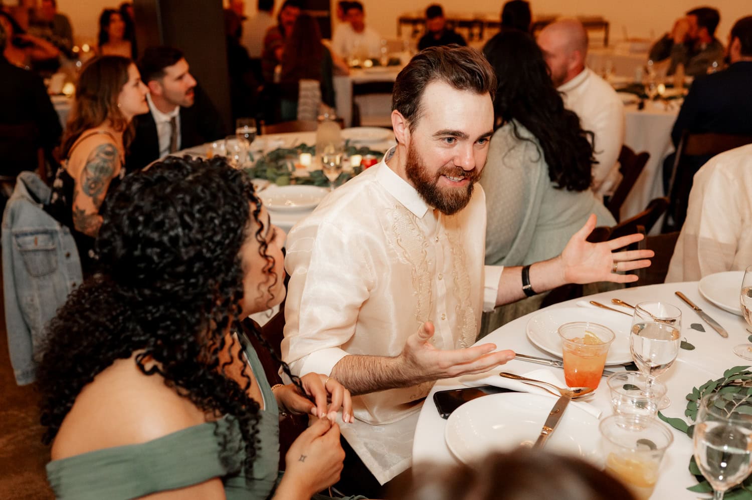 Guests seated around a table at a Union/Pine wedding, engaged in animated conversation while enjoying their drinks.