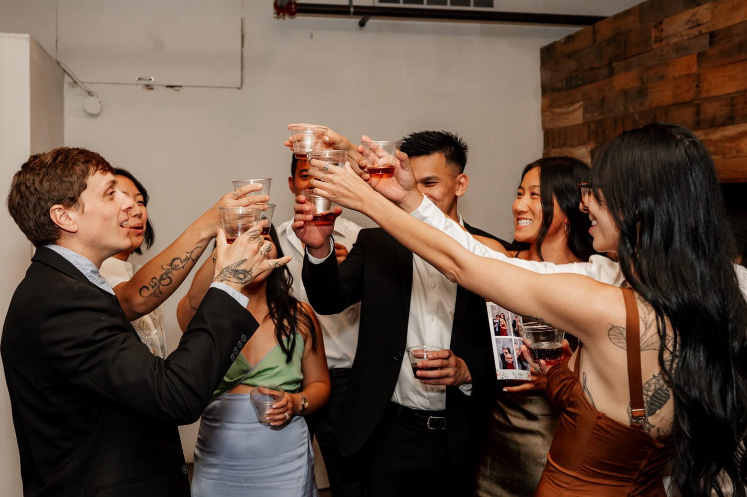 A group of people in formal attire at a wedding at Union/Pine is raising their glasses in a celebratory toast, capturing the joy of the gathering.