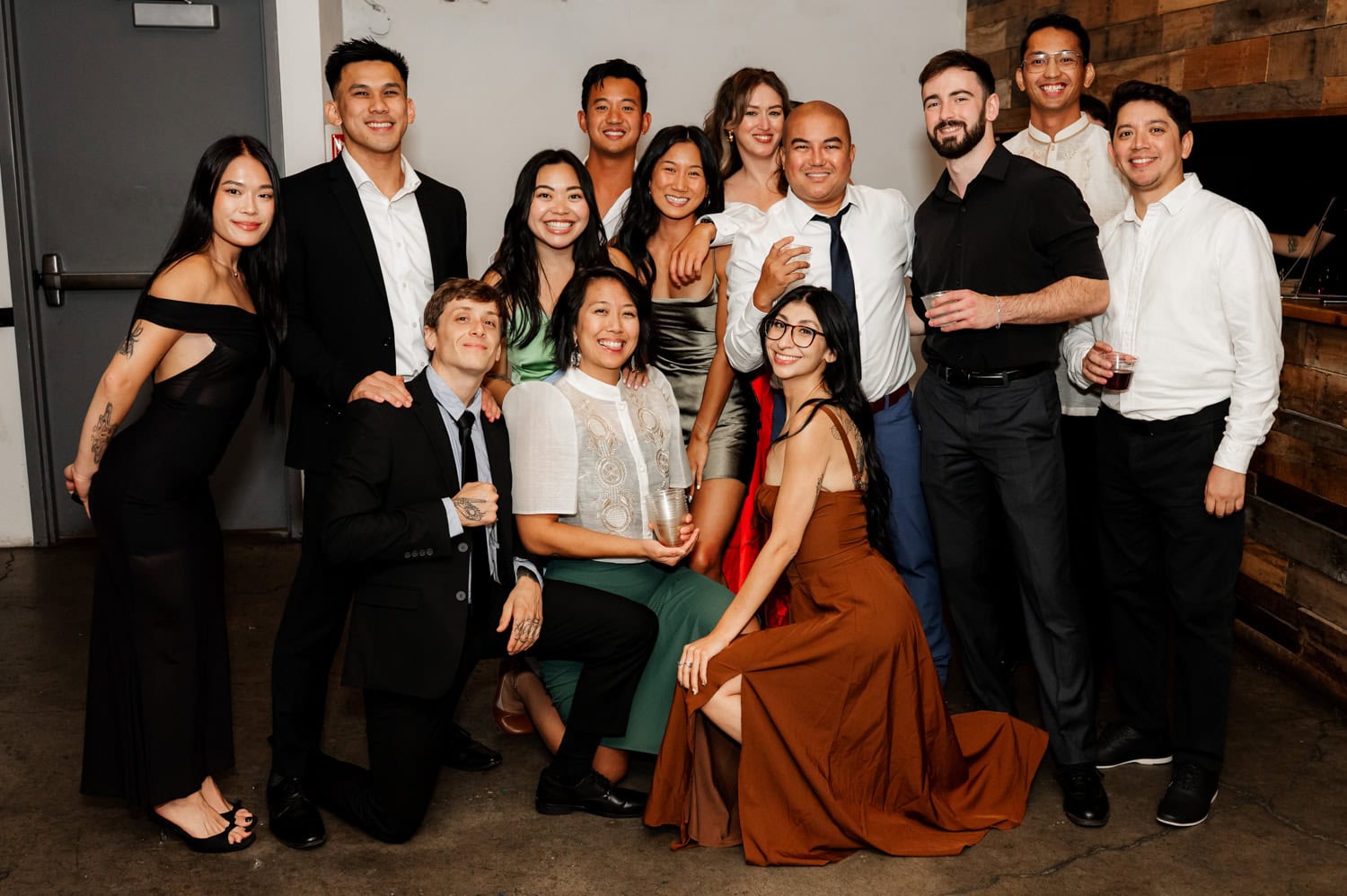 A group of people dressed in formal attire stand together, smiling warmly for a photo at a wedding taking place at Union/Pine.