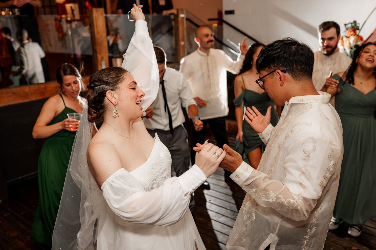The bride and groom joyfully dance with guests at the wedding reception inside Union/Pine, surrounded by smiling faces.