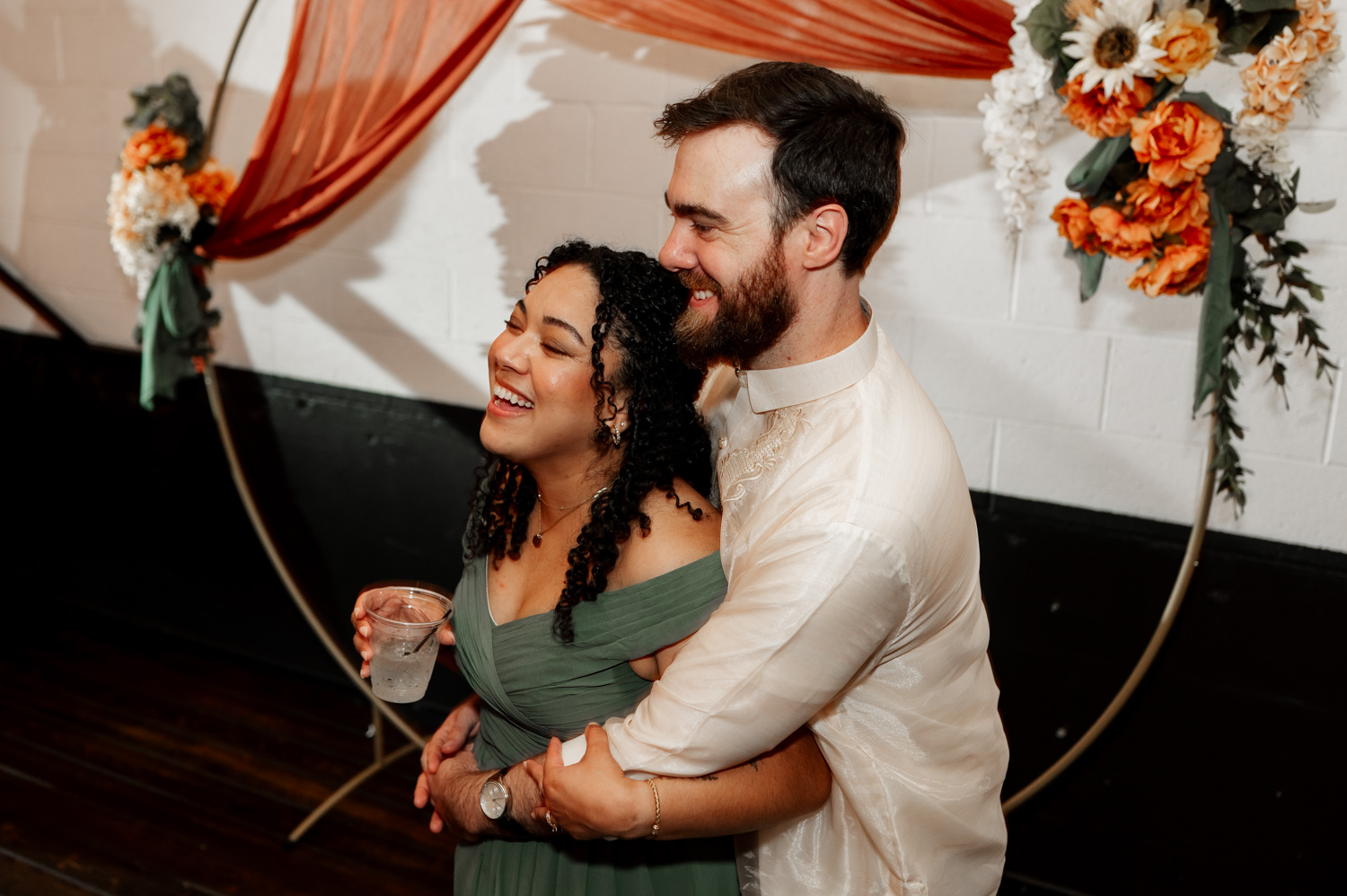 A couple smiling and embracing at a wedding at Union/Pine, surrounded by elegant floral and fabric decorations indoors.
