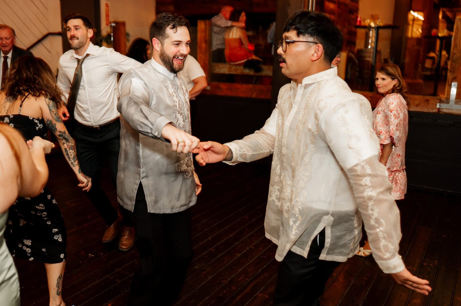 People dancing joyfully on a wooden floor at Union/Pine, wearing traditional barong attire, smiling and holding hands.