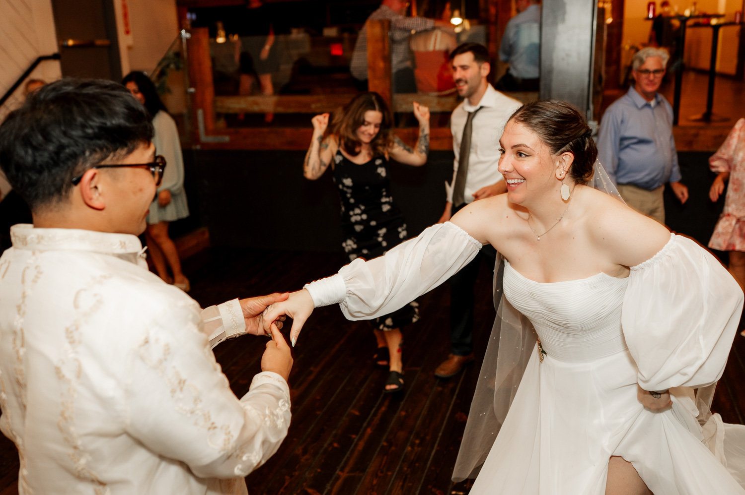 A bride and groom dance joyfully on the wooden floor of Union/Pine, surrounded by smiling guests.